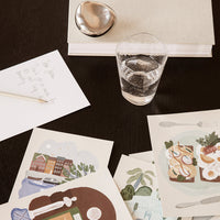 Colorful illustrated prints with soft pastel tones, featuring abstract patterns and whimsical designs on a dark tabletop.