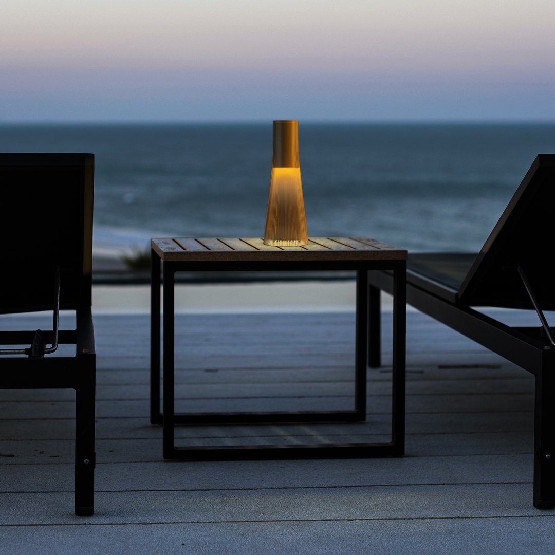 Golden lamp on a sleek black table, with ocean blue and soft purple hues in the background at sunset.