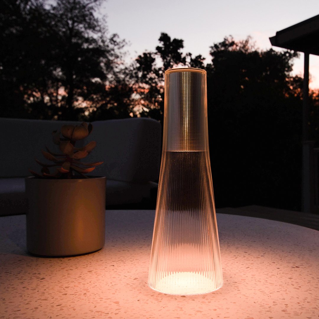 Transparent glass lantern with a sleek, modern shape emitting warm light against a twilight backdrop.