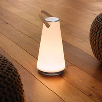 White conical lamp with a wooden handle on a wooden floor, featuring smooth surfaces and soft, glowing light.