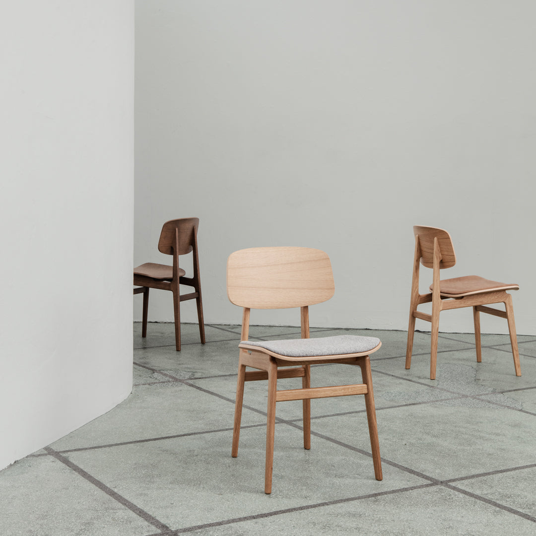 Neutral-toned wooden chairs featuring smooth lines and minimalist design against a sleek concrete floor backdrop.