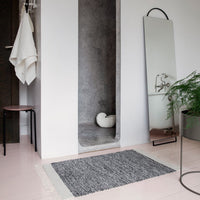 Gray and white woven rug with a textured pattern, placed on a pink floor in a modern bathroom setting.