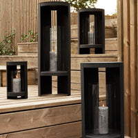 Black candle holders with geometric patterns, showcasing a modern design on wooden outdoor surfaces.