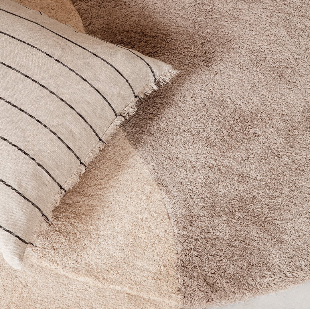 Beige and taupe shag rug with a striped beige pillow, creating a cozy neutral-toned decor.