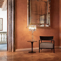 Elegant gray and black patterned chair beside a sleek glass lamp on a round black table against warm terracotta walls.
