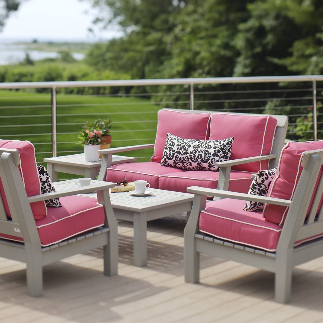 Pink outdoor furniture set with black and white patterned cushions, set on a light wooden deck with lush green surroundings.