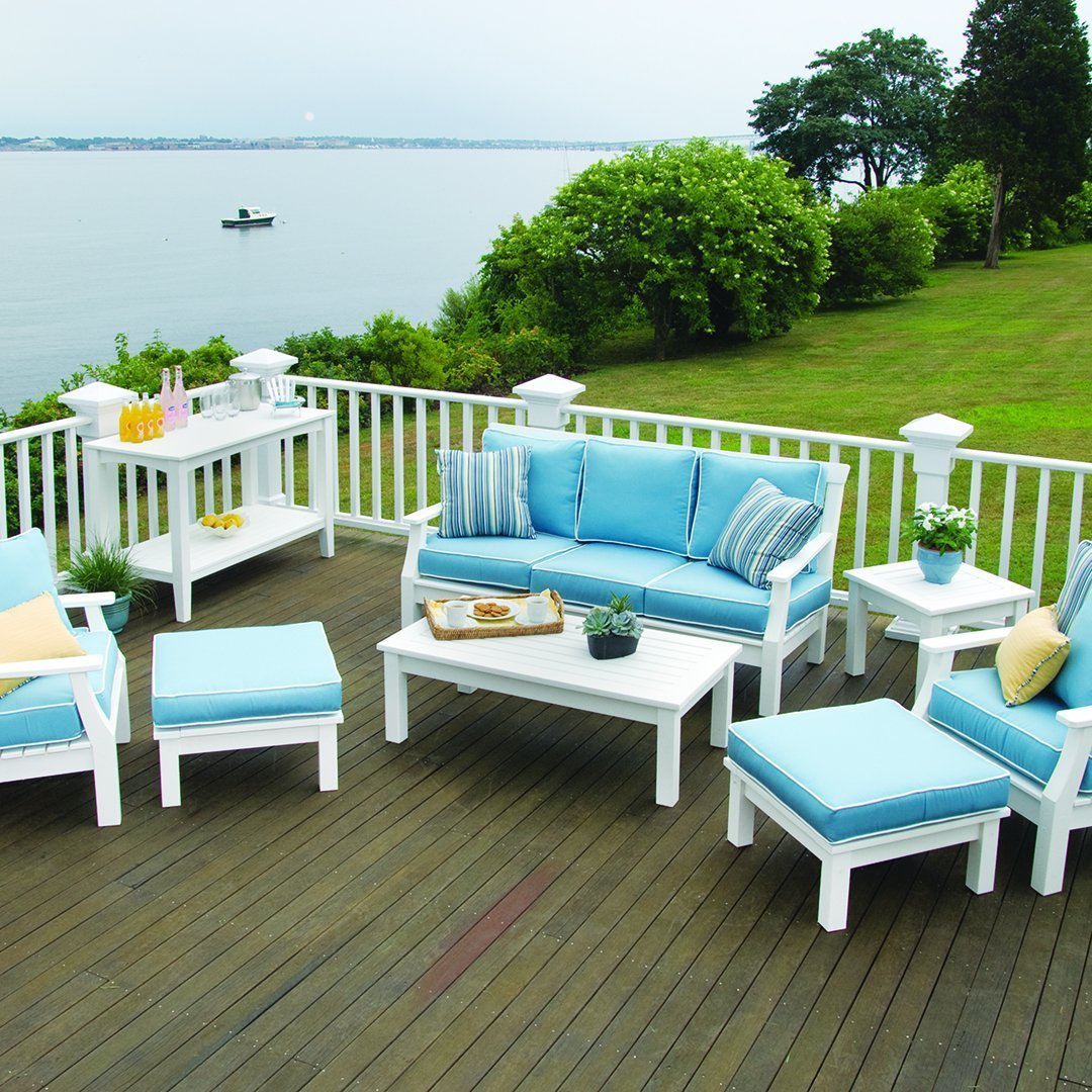 Light blue cushions on white patio furniture, set against a green landscape and calm water backdrop.