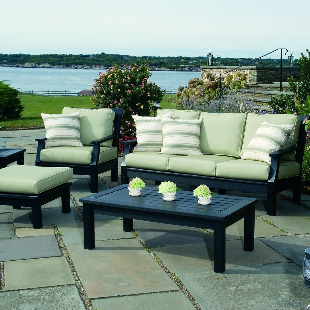 Black outdoor furniture with light green cushions and striped accent pillows, set against a scenic waterfront backdrop.