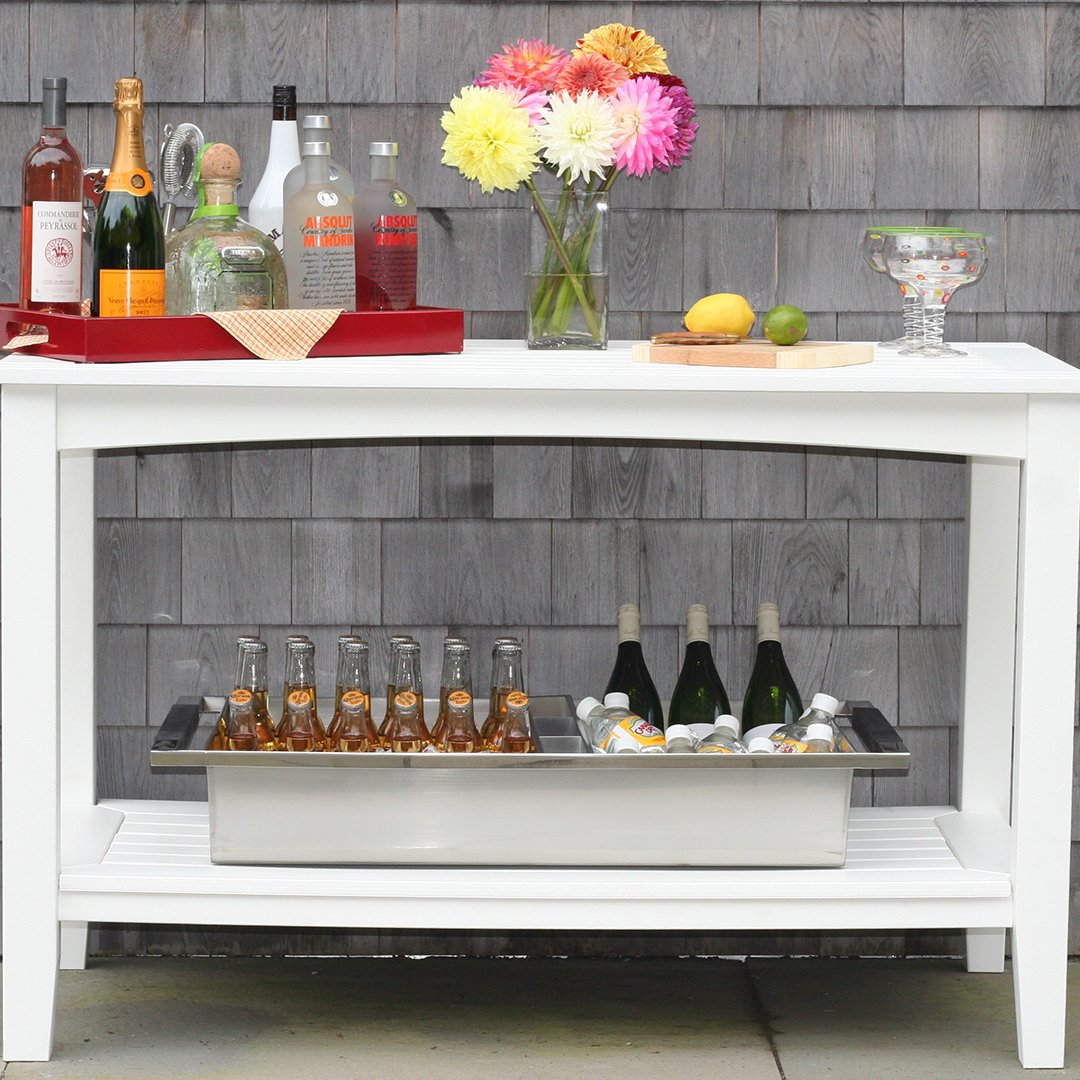 "White outdoor bar with colorful floral arrangement and patterned bottles on a gray wooden backdrop."