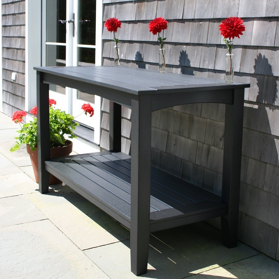 Dark gray outdoor table with a slatted design, complemented by vibrant red flowers in pots.