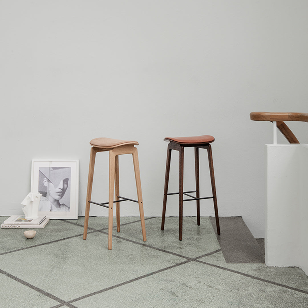 "Light wood and dark wood bar stools on a textured green floor, featuring smooth finishes and simple lines."