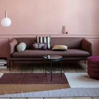 Modern brown sofa with patterned pillows on a pastel pink wall, complemented by a geometric rug and stylish coffee table.