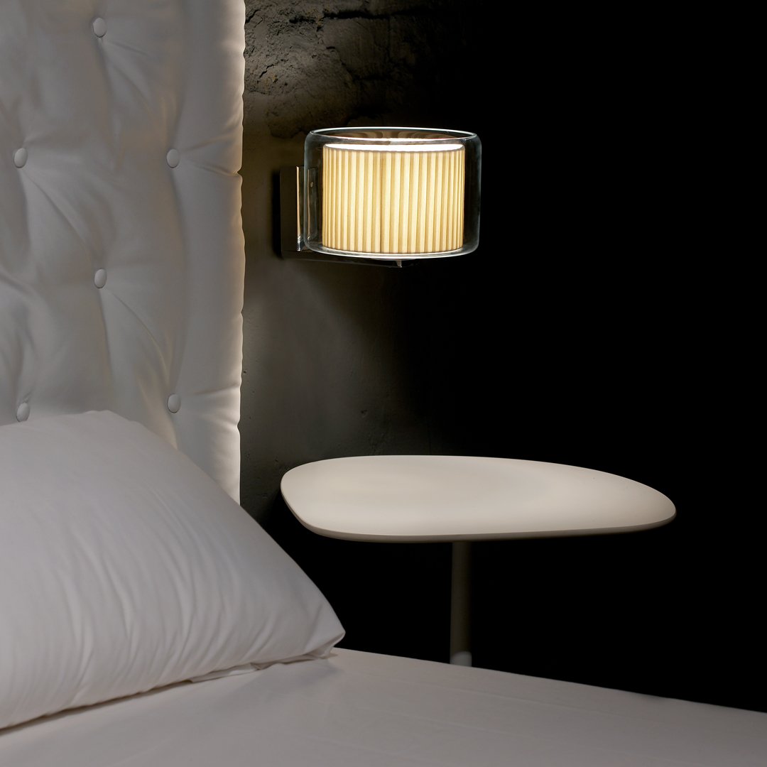 Beige striped lampshade against a black wall, with a sleek white nightstand and plush white bedding.