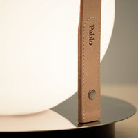 Close-up of a beige leather strap on a round white lamp, set against a sleek black base.