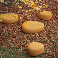 "Set of smooth, rounded, mustard-yellow outdoor seating cushions on a bed of autumn leaves."