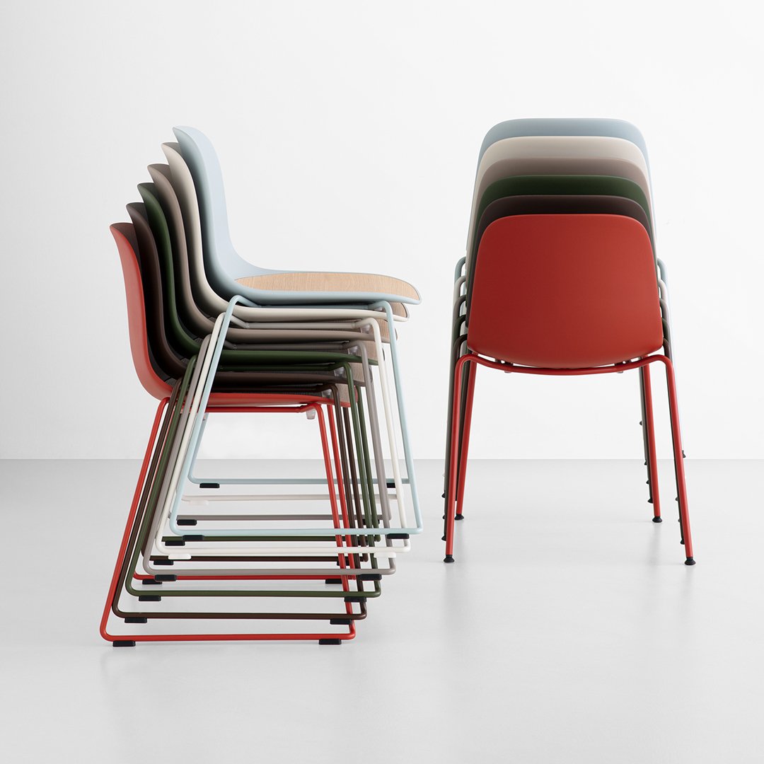 Stacked chairs in muted tones: light blue, green, beige, and vibrant red, showcasing a modern design and sleek metal frames.