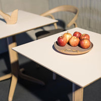 Modern white tabletop with a wooden base, featuring a round wooden plate of vibrant red apples.