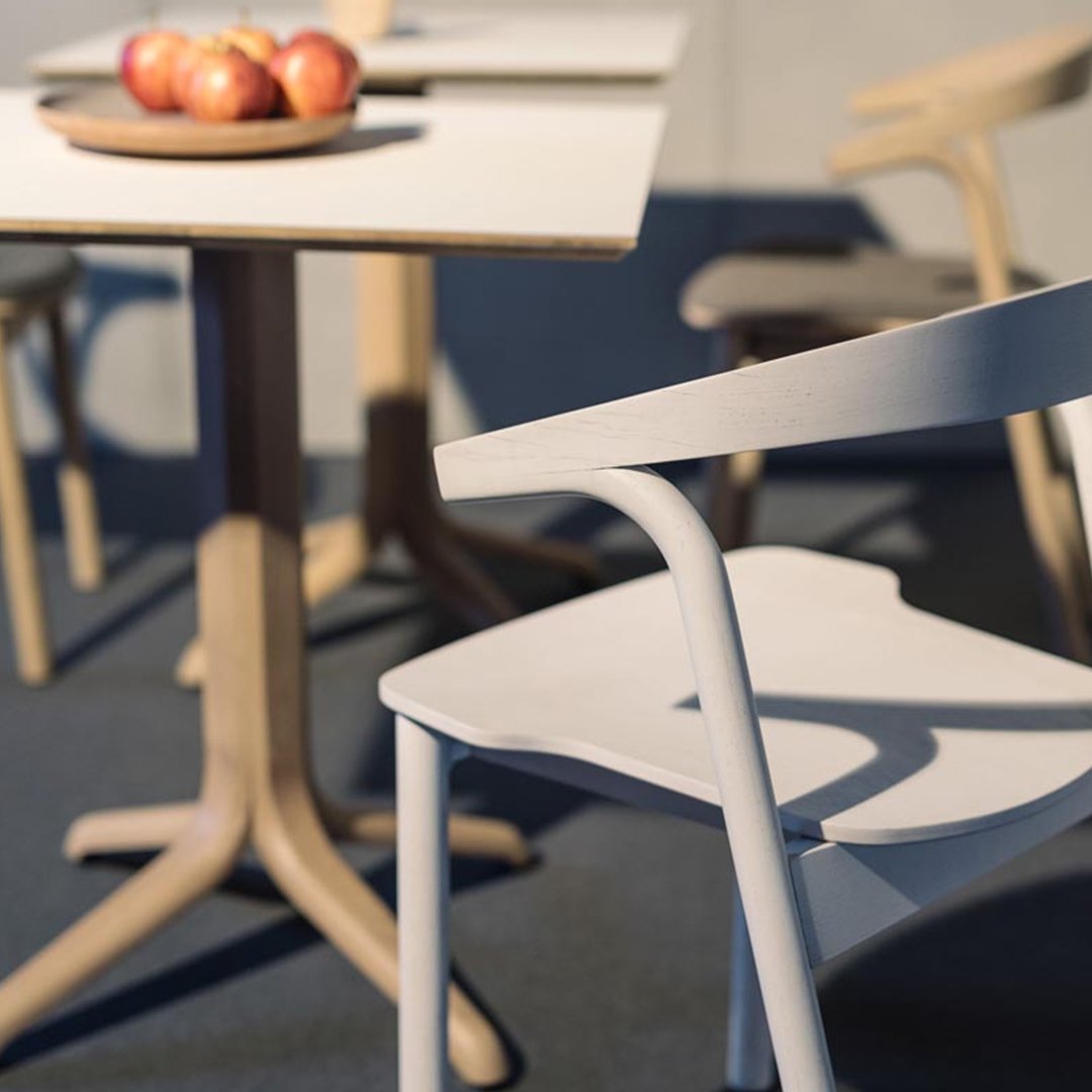 Modern light gray chair with smooth lines, set against a minimalist wooden table and navy blue floor.