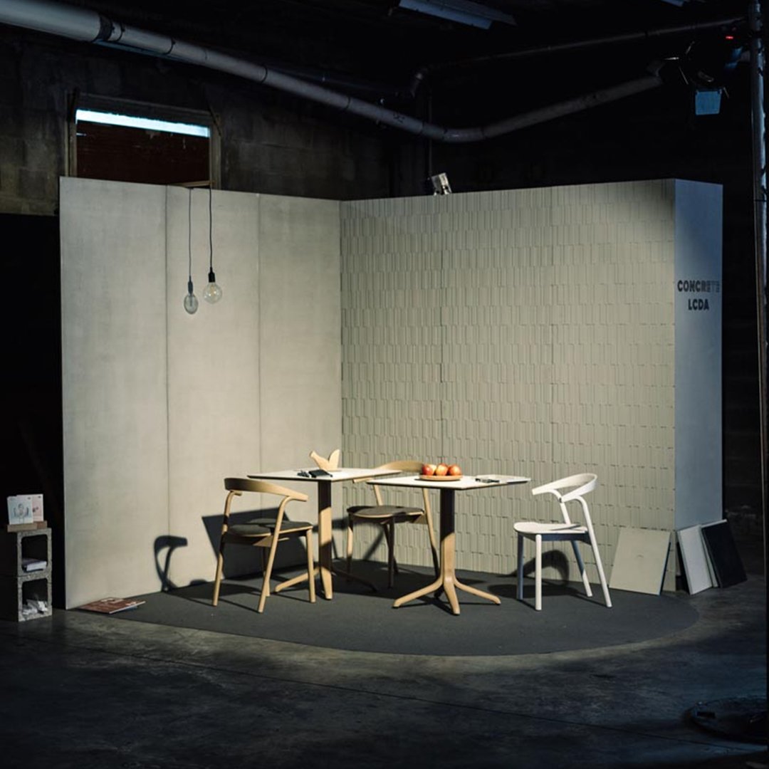 Minimalist grey walls with subtle texture, light wood furniture, and black flooring create a modern, stylish setting.