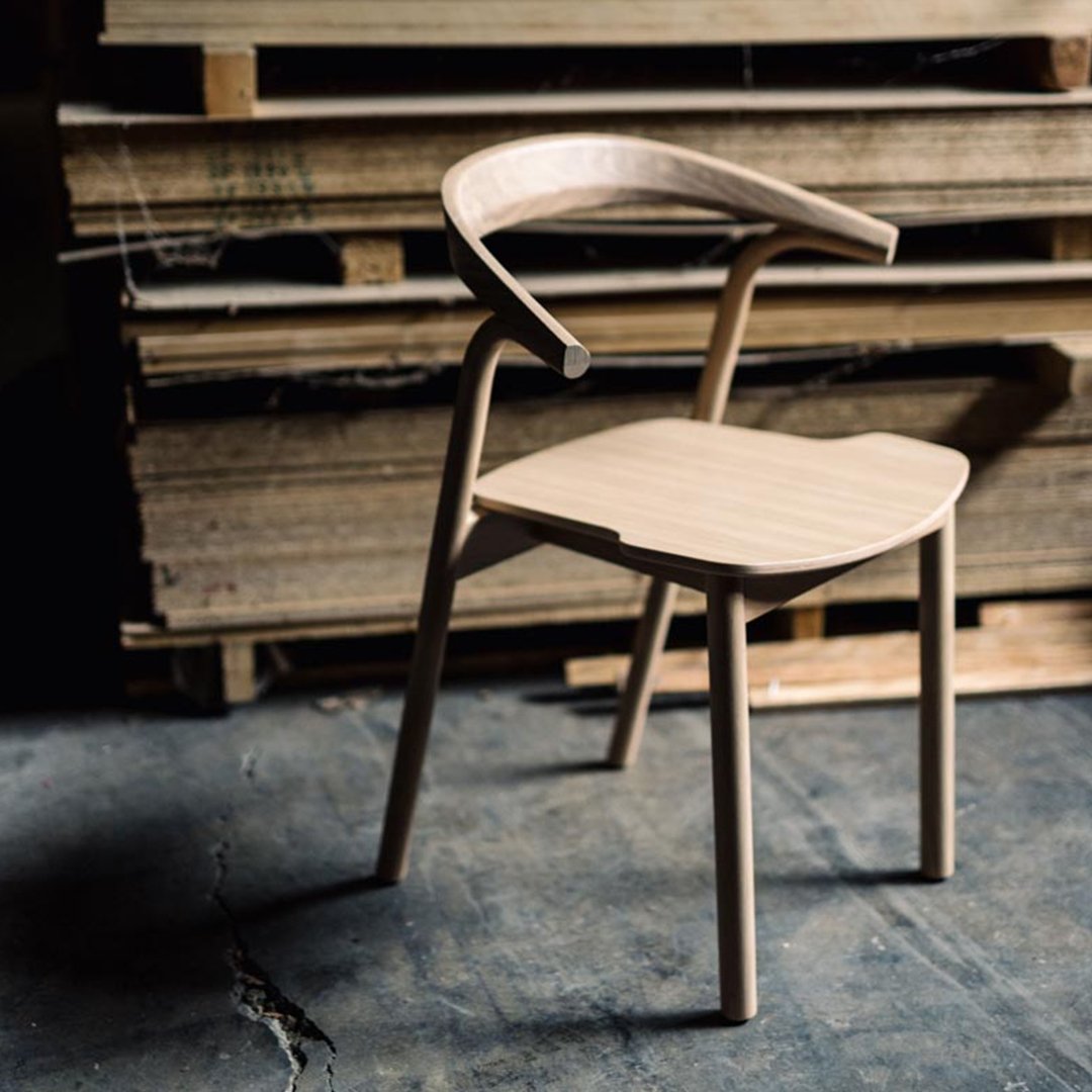 Light natural wood chair with smooth lines and contemporary design against a rustic wooden backdrop.