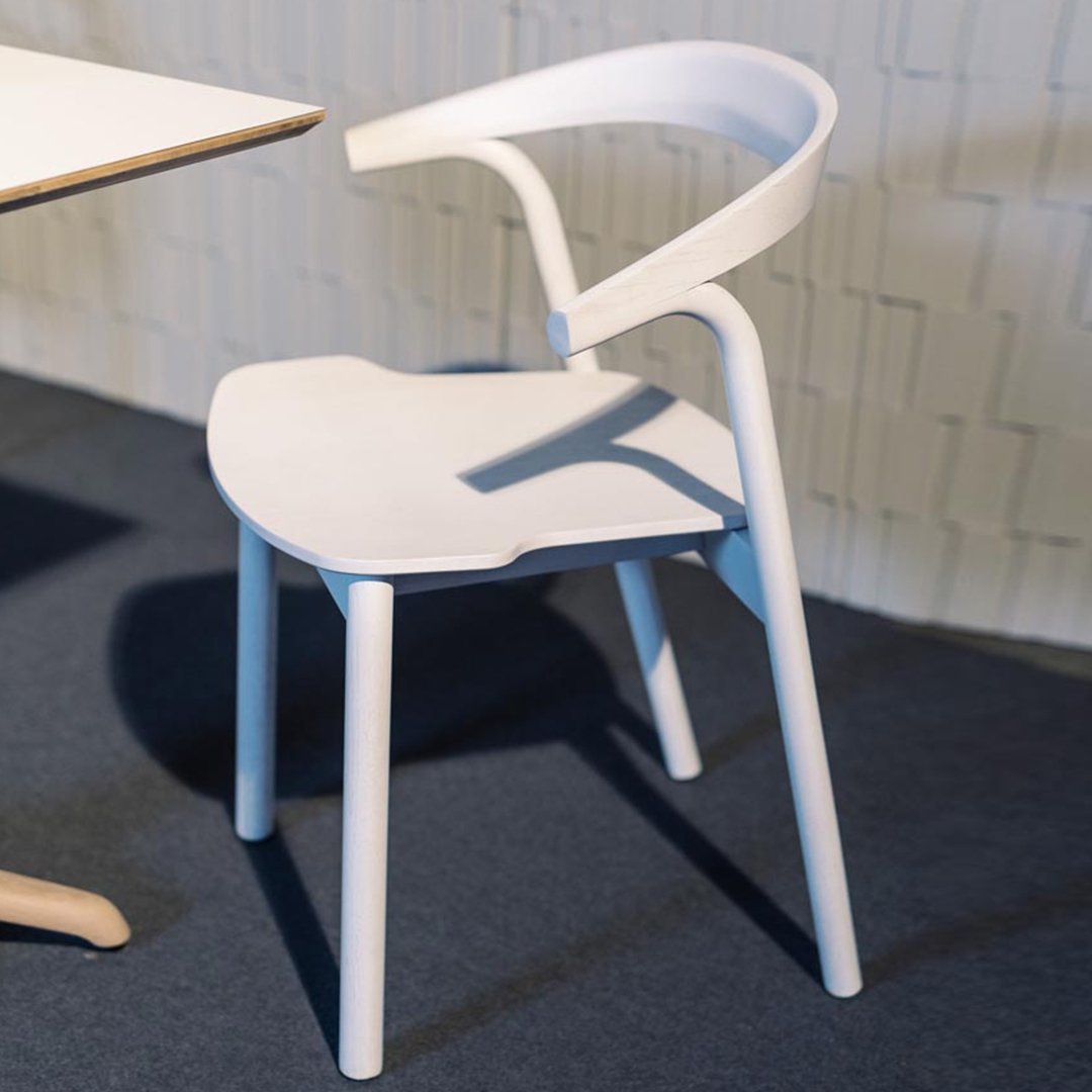 White modern chair with a minimalist design and smooth, curved lines against a dark carpeted floor.