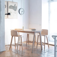 Light wood dining table and stools in a bright, minimalist space with white walls and natural light.