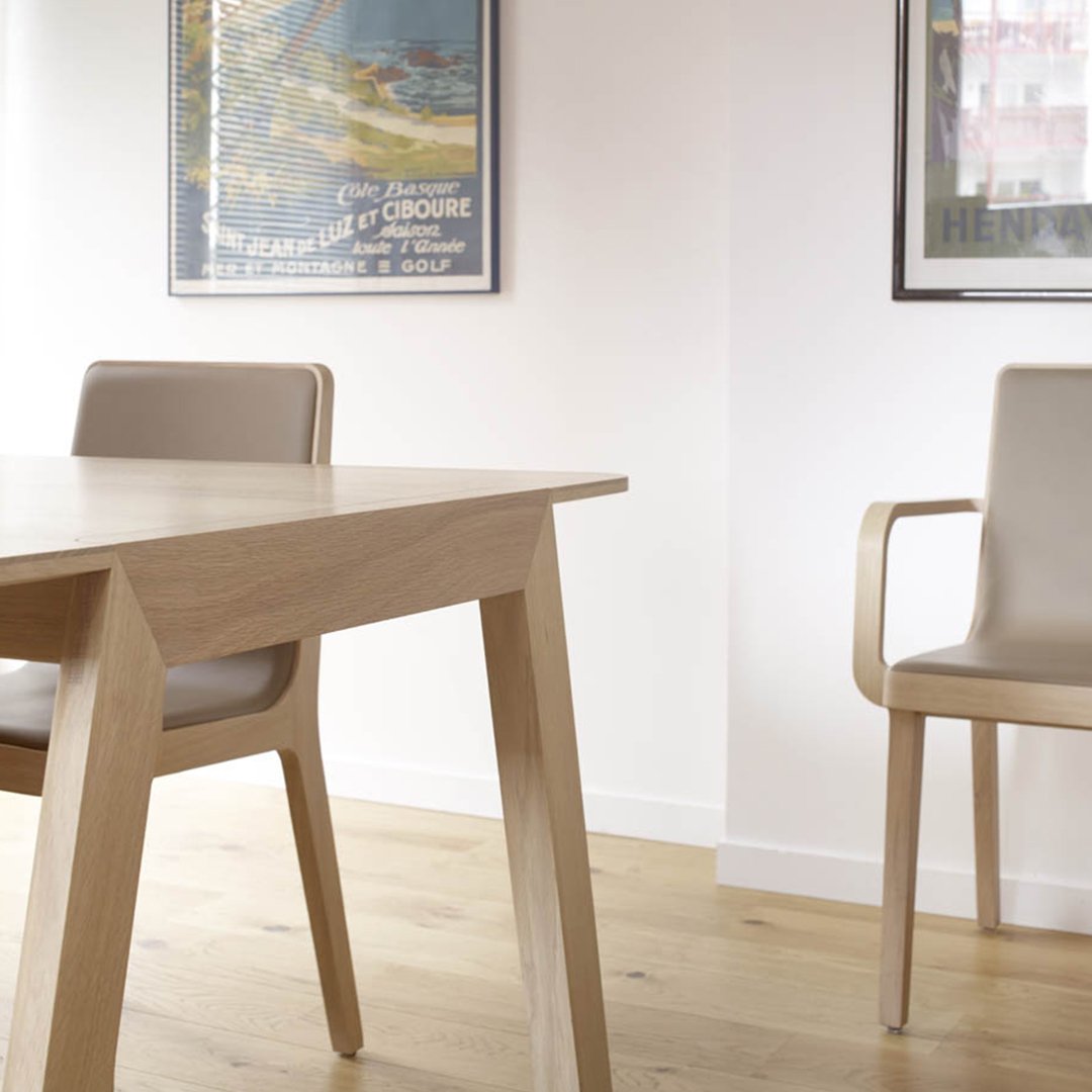 Light wood dining table with beige chairs in a minimalist room featuring subtle artwork and warm wooden flooring.
