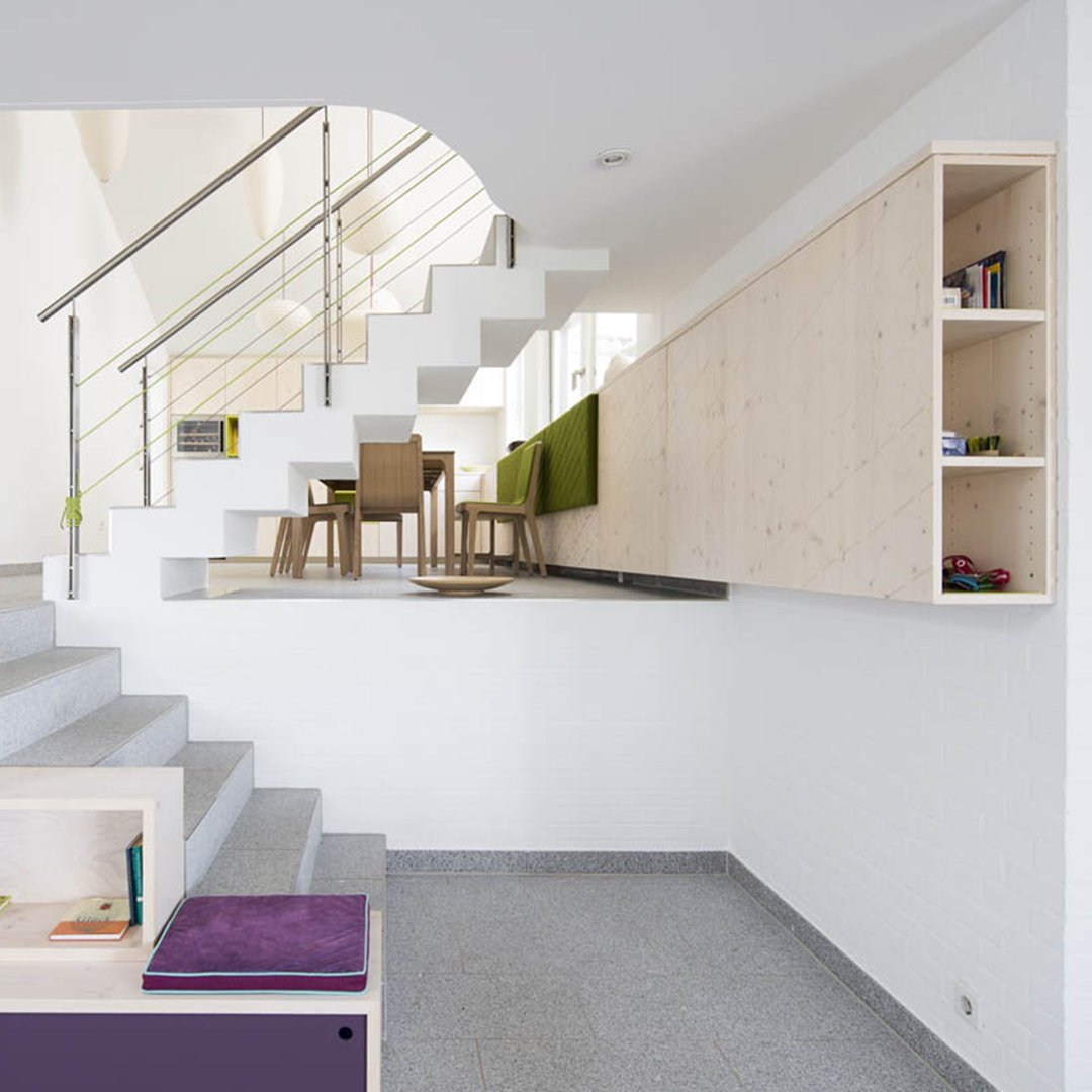 Modern staircase with white walls, light wood accents, and a geometric pattern in gray tiles. Vibrant purple and green elements.
