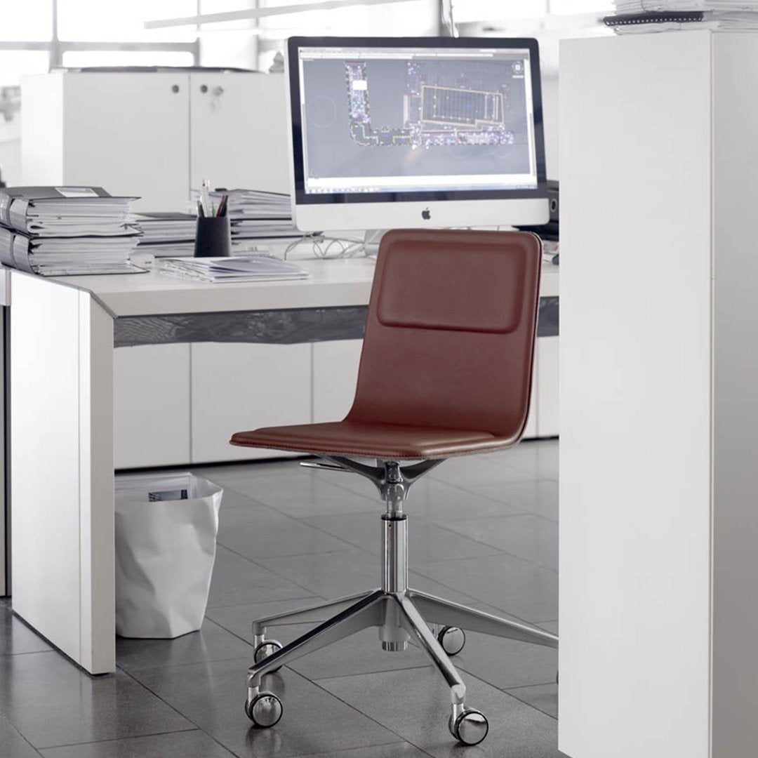 Brown leather office chair with a sleek, minimalist design and chrome wheels, set against a modern workspace backdrop.