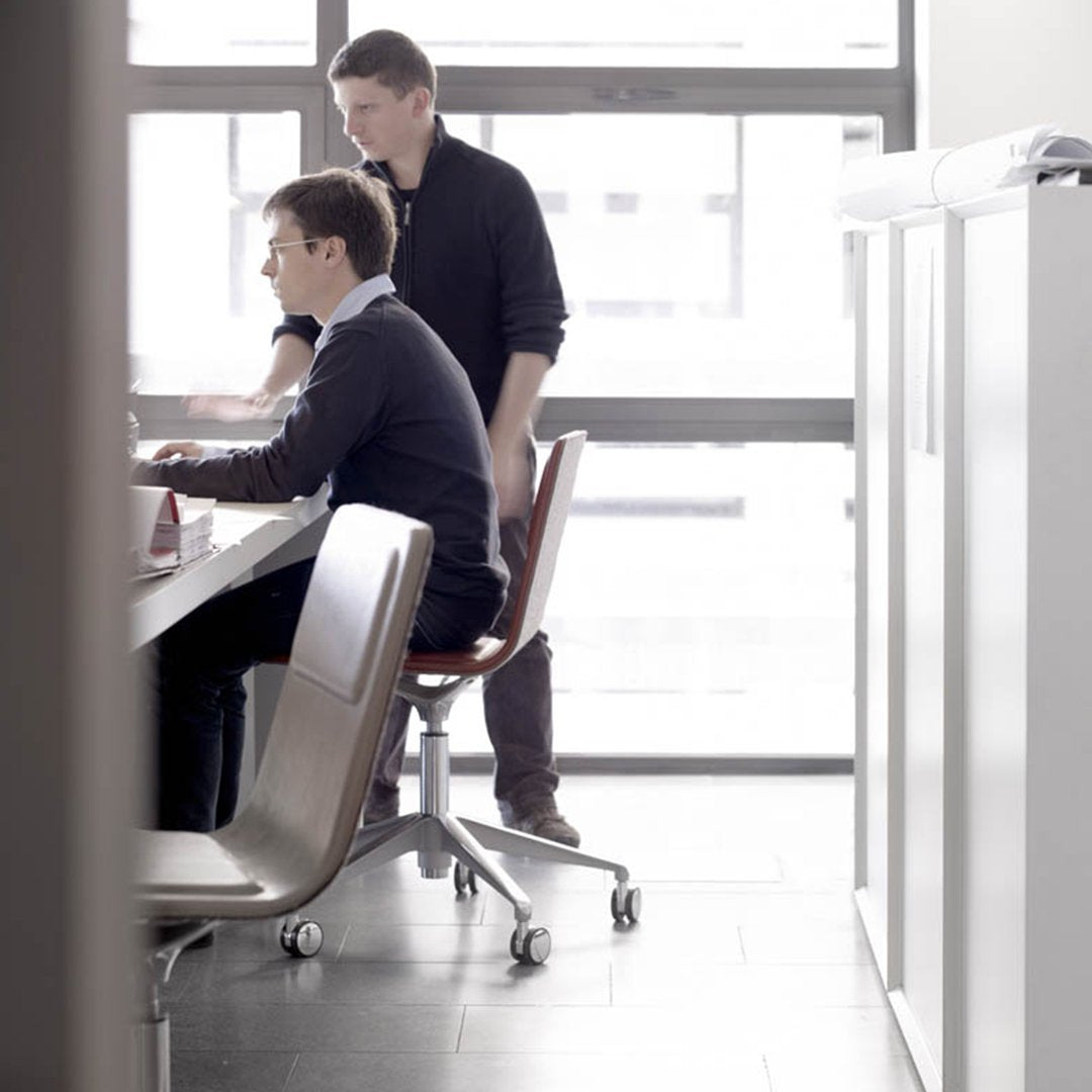 Two professionals at a modern office desk, featuring sleek gray chairs and a minimalist workspace.