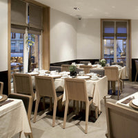 Modern dining room with neutral beige tones, light wooden furniture, and white tablecloths, creating an inviting ambiance.