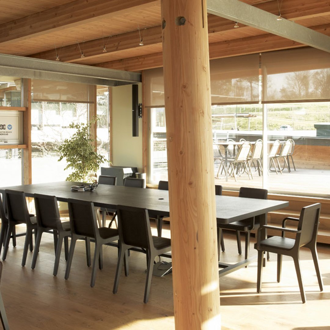 Modern conference room with wooden beams, sleek black chairs, and light-filtering beige blinds, creating a warm, inviting atmosphere.