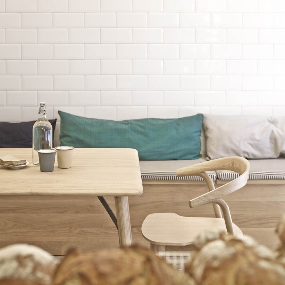 Light wood table with soft blue, teal, and gray cushions against a white tiled wall, creating a modern, cozy vibe.