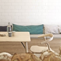Light wood table with soft blue, teal, and gray cushions against a white tiled wall, creating a modern, cozy vibe.