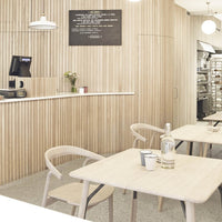 Wooden slat wall with light natural tones, minimalist tables, and white accents create a warm, inviting café atmosphere.
