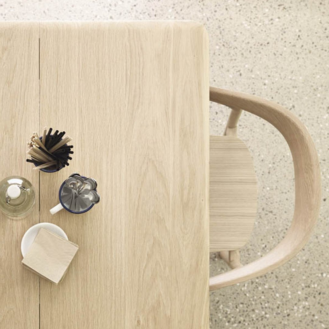 Light wood table with natural grain, paired with minimalist ceramic and glass decor on a speckled floor.