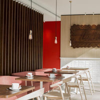Modern cafe interior with red accent wall, wooden paneling, and light-colored furniture featuring subtle geometric patterns.