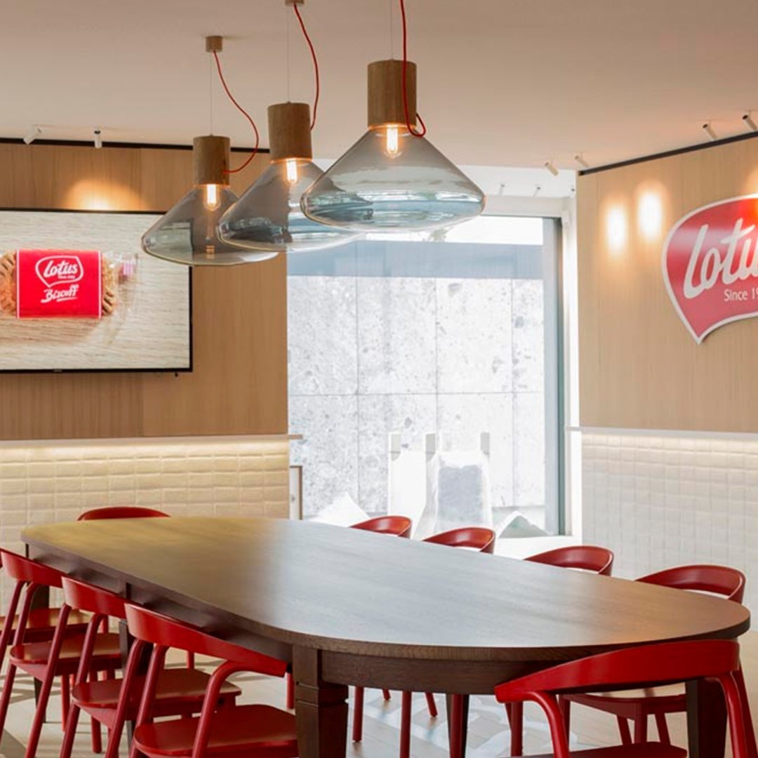 Modern dining space featuring a wooden table, red chairs, and sleek glass pendant lights against a neutral backdrop.
