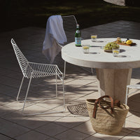 White wire chair with a sleek design, round stone table, and natural woven basket create a modern outdoor setting.