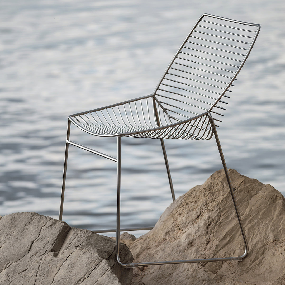 Sleek gray wire chair with modern striped design, set against a serene water backdrop. Perfect for stylish outdoor decor.