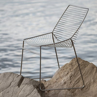 Sleek gray wire chair with modern striped design, set against a serene water backdrop. Perfect for stylish outdoor decor.