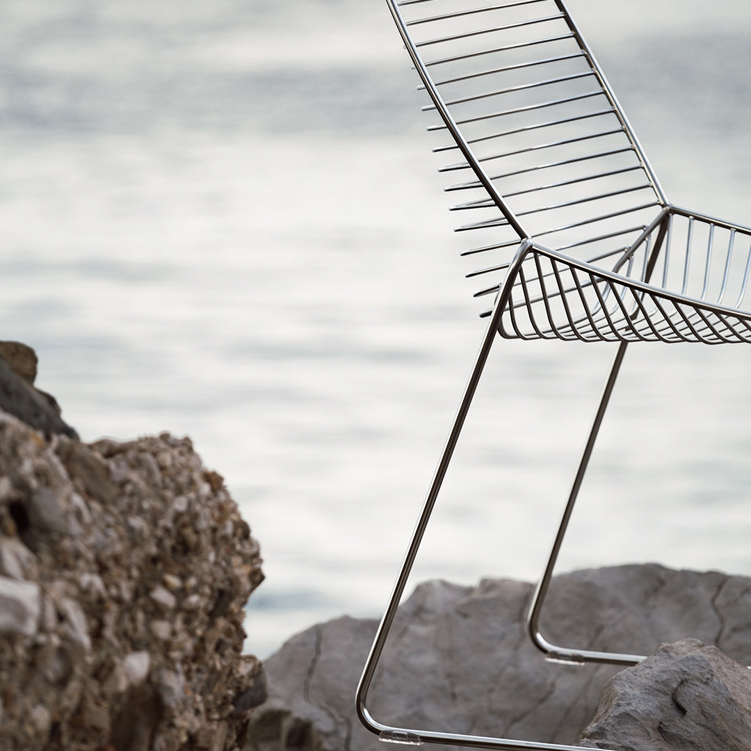 Sleek metal chair with a minimalist chrome finish, featuring string-like seat patterns against a natural rocky background.