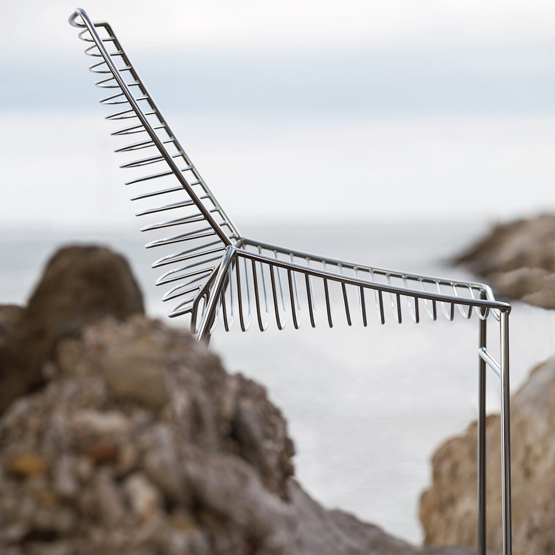 Silver metal chair with a unique spiked pattern, set against a serene coastal backdrop.