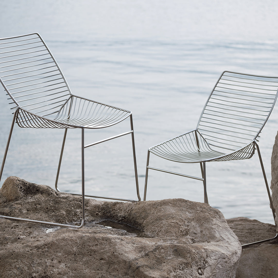 "Contemporary wire chairs in sleek silver finish, featuring linear patterns and minimalist design against a natural backdrop."