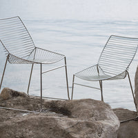 "Contemporary wire chairs in sleek silver finish, featuring linear patterns and minimalist design against a natural backdrop."