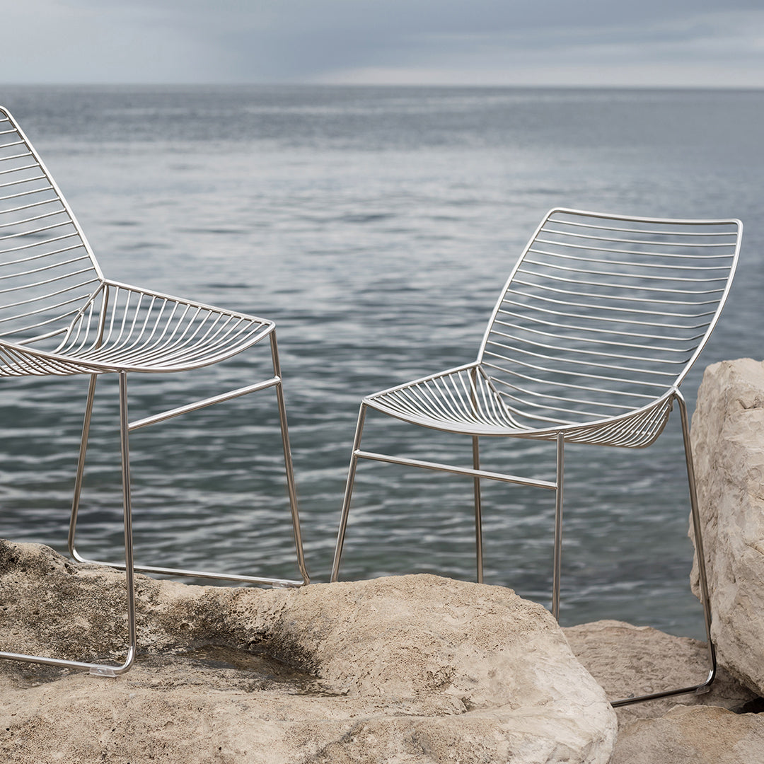 "Minimalist wire chairs with sleek silver finish, featuring an elegant open pattern against a serene coastal backdrop."