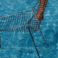 "Modern wire chair in shimmering silver against a vibrant blue water background."