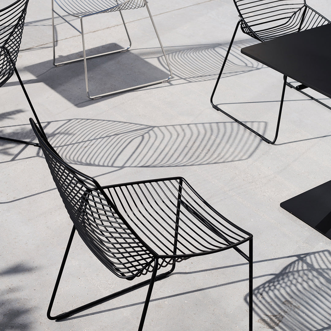 Stylish black wire chairs with geometric patterns casting shadows on a light gray surface. Modern outdoor furniture design.