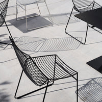 Stylish black wire chairs with geometric patterns casting shadows on a light gray surface. Modern outdoor furniture design.