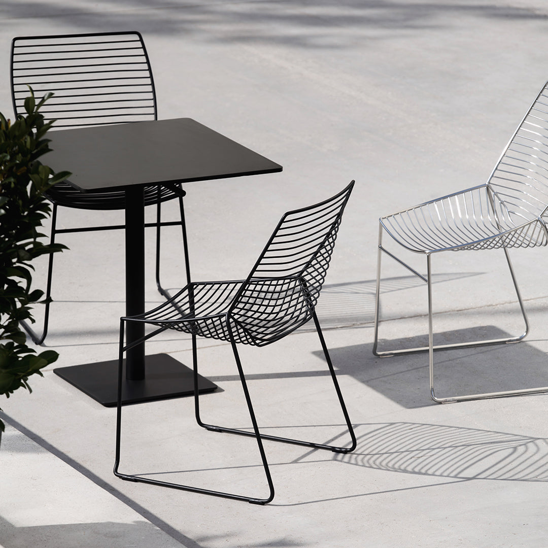 Black metal table with three wireframe chairs in black and white, featuring sleek, modern lines and minimalist design.
